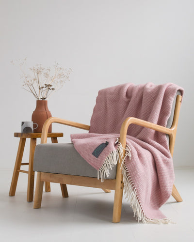 Large pink herringbone wool blanket draped over grey lounge chair.