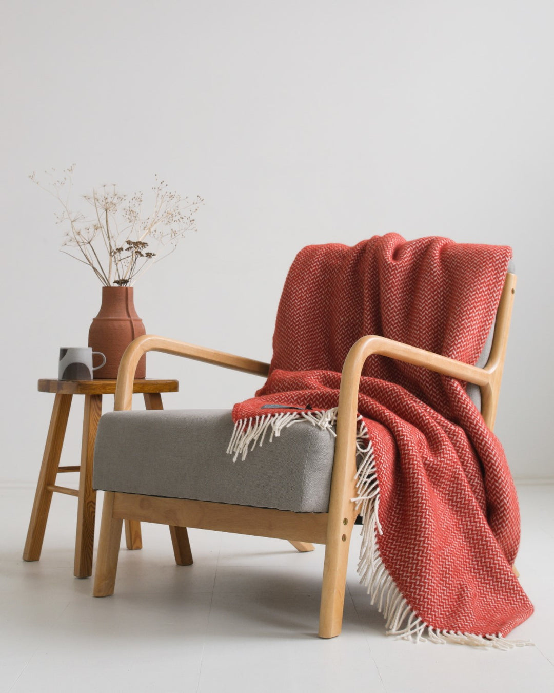 Large red herringbone wool blanket draped over a grey lounge chair