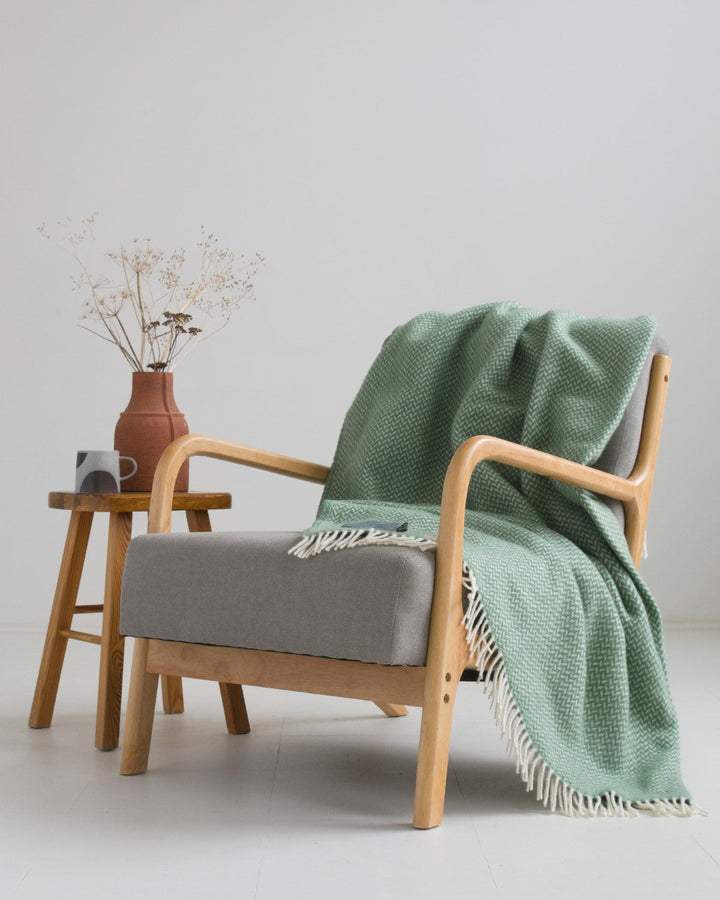 Extra large green herringbone wool blanket draped over a lounge chair