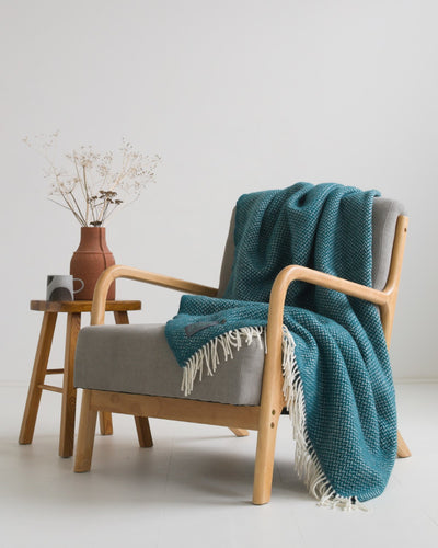 A green herringbone wool blanket draped over a lounge chair. 