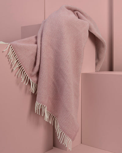 An extra large pink herringbone wool throw draped over display plinths