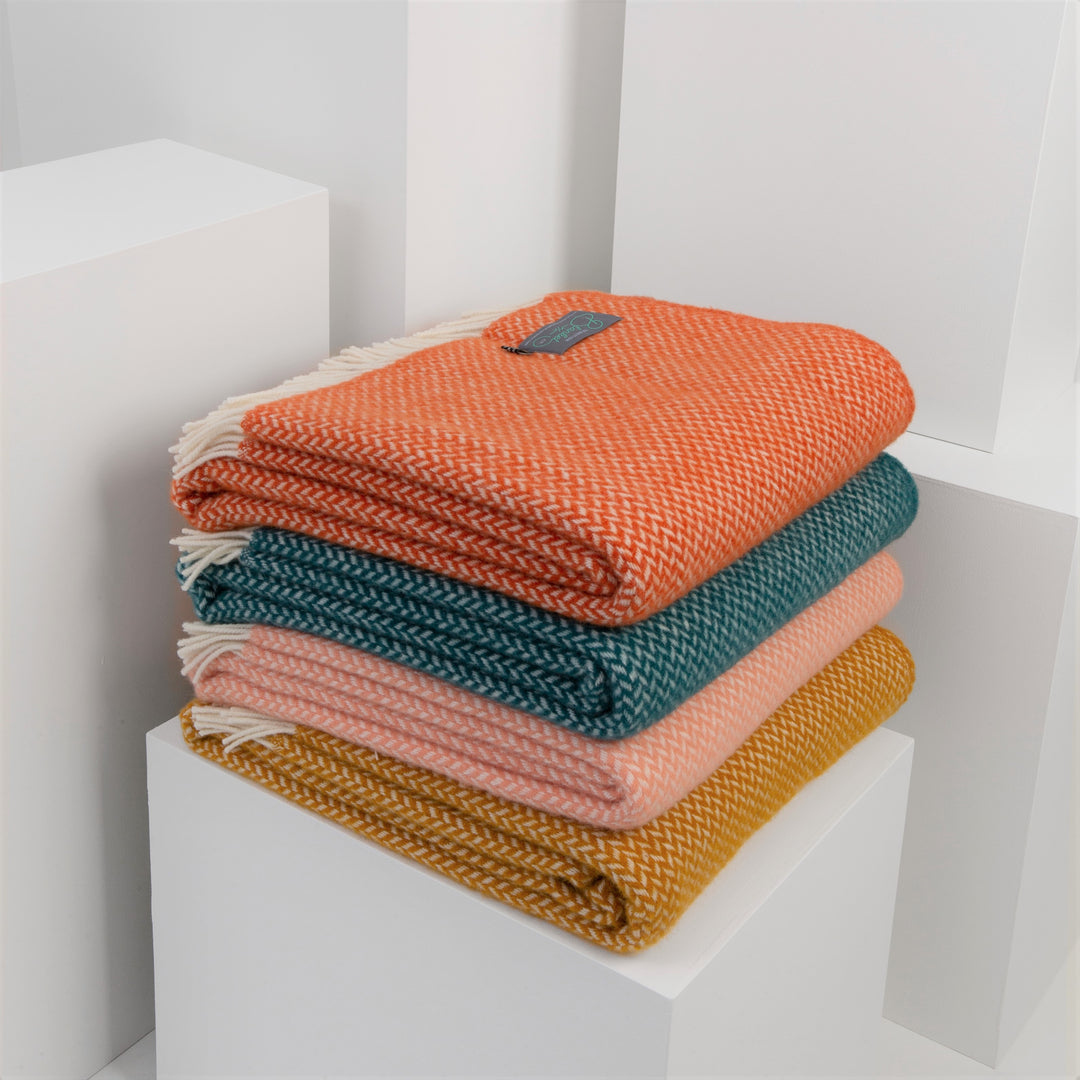 A stack of folded wool blankets in orange, green, pink, and yellow on a display plinth
