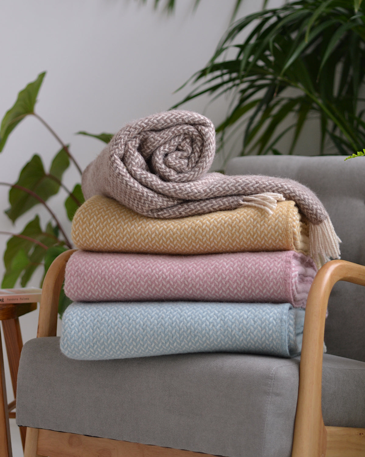 Four folded wool blankets stacked on a grey lounge chair.