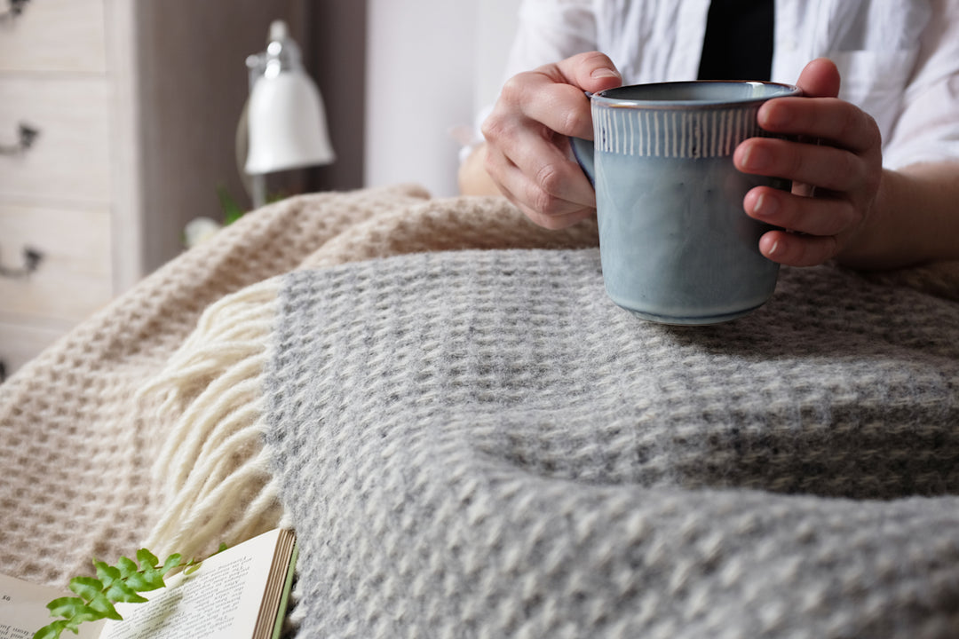 A person holding a mug over an extra large grey waffle wool blanket