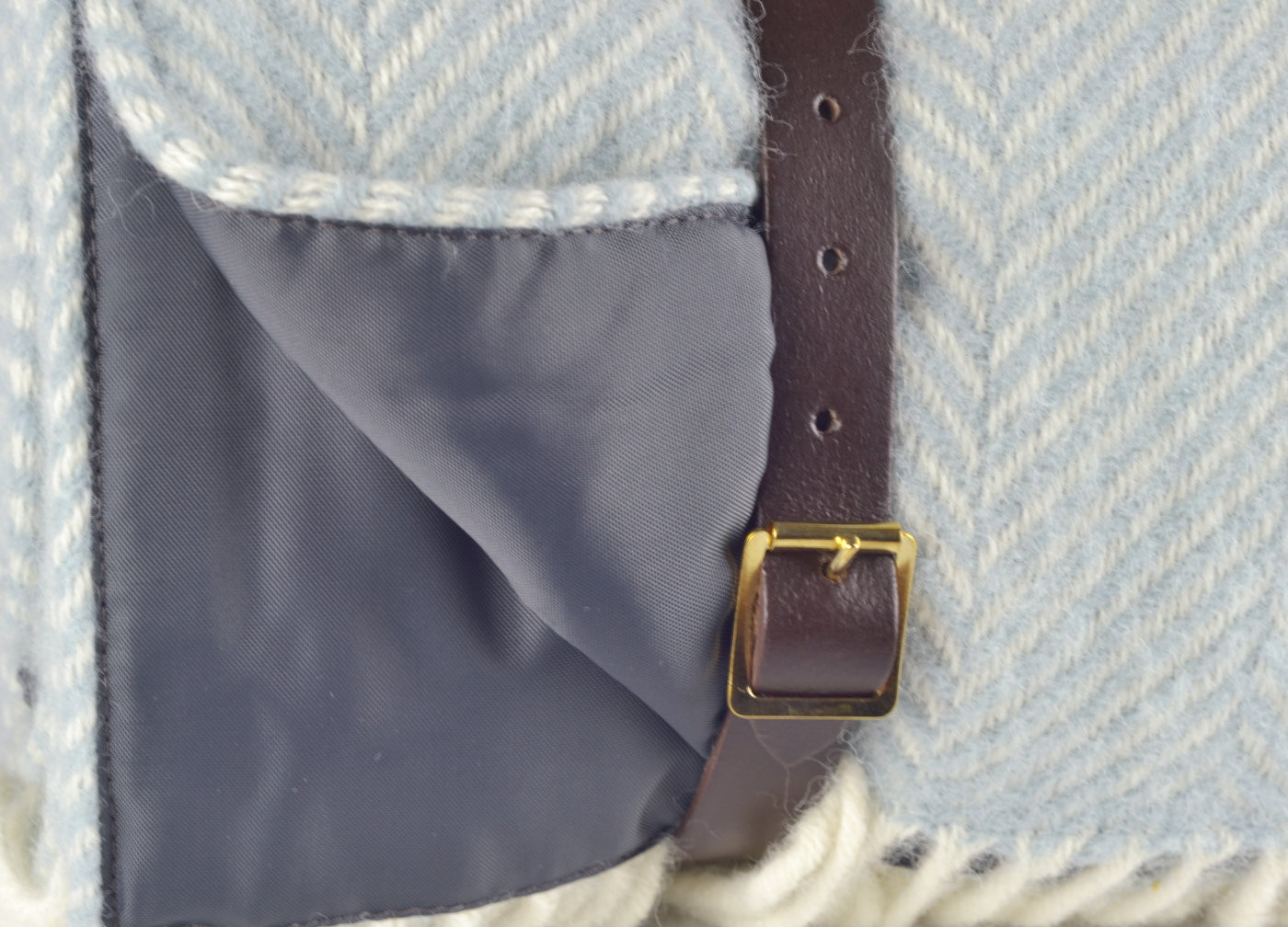 Closeup of leather strap wrapped around a blue wool picnic rug.