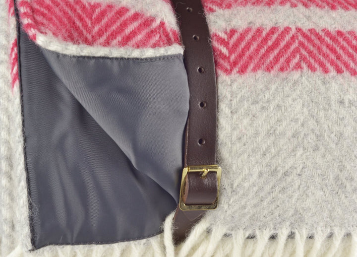 Closeup of leather strap wrapped around a grey and red wool picnic rug by The British Blanket Company.