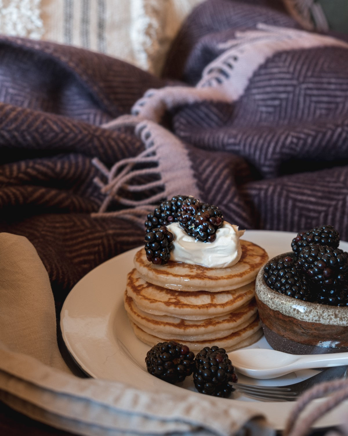 A stack of pancakes with blackberries placed on top of a purple wool blanket.