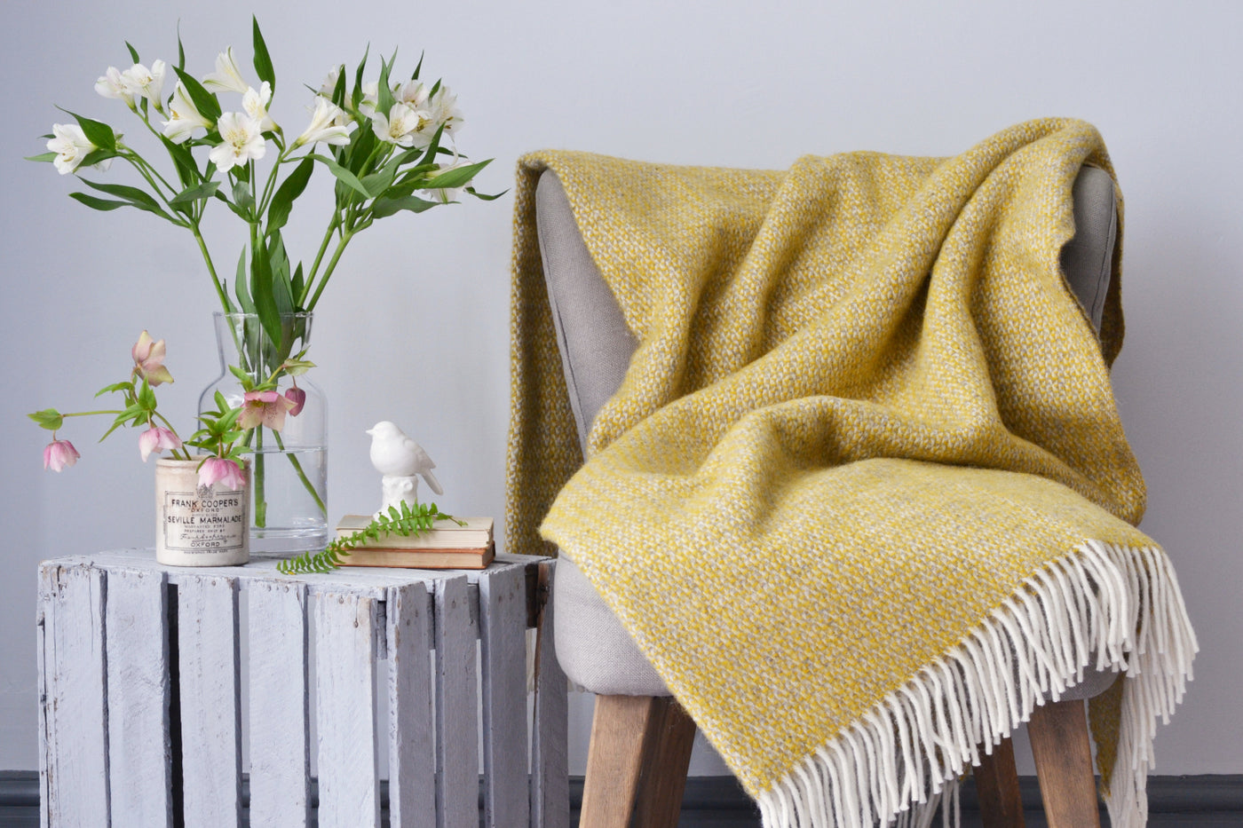 A large yellow and grey windmill wool blanket draped over a lounge chair on the right. Flower cases placed on a wooden crate on the left