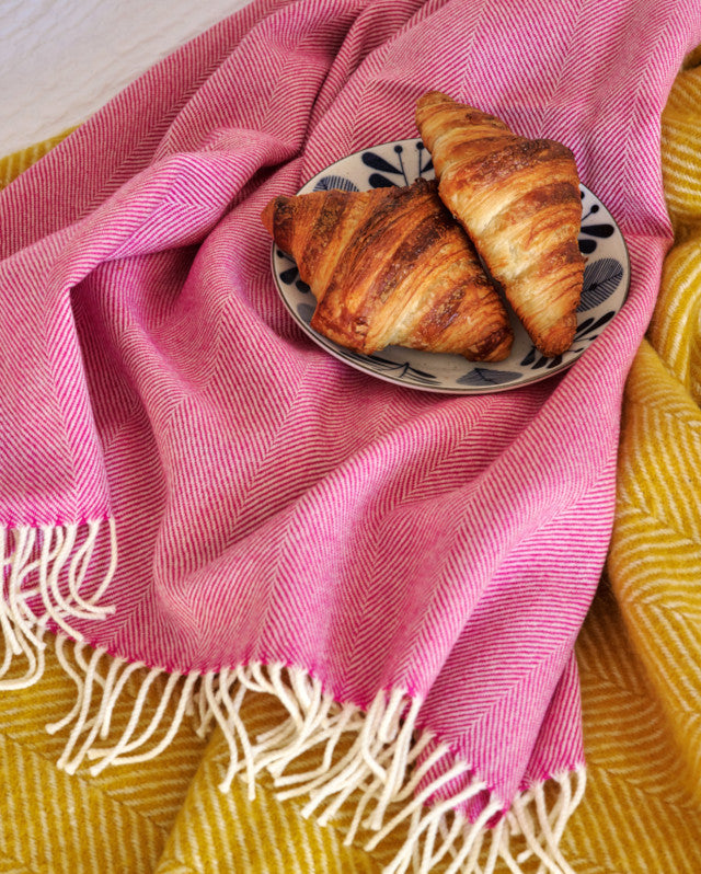 breakfast in bed scene with two croissants on a plate and pink merino wool throw blanket by The British Blanket Company online shop