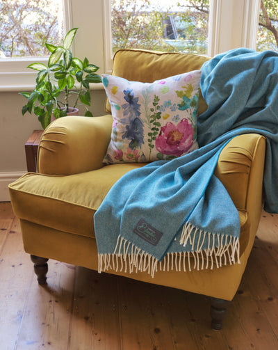 yellow velvet armchair styled with a floral cushion and bright cornish blue merino wool throw blanket by The British Blanket Company online shop