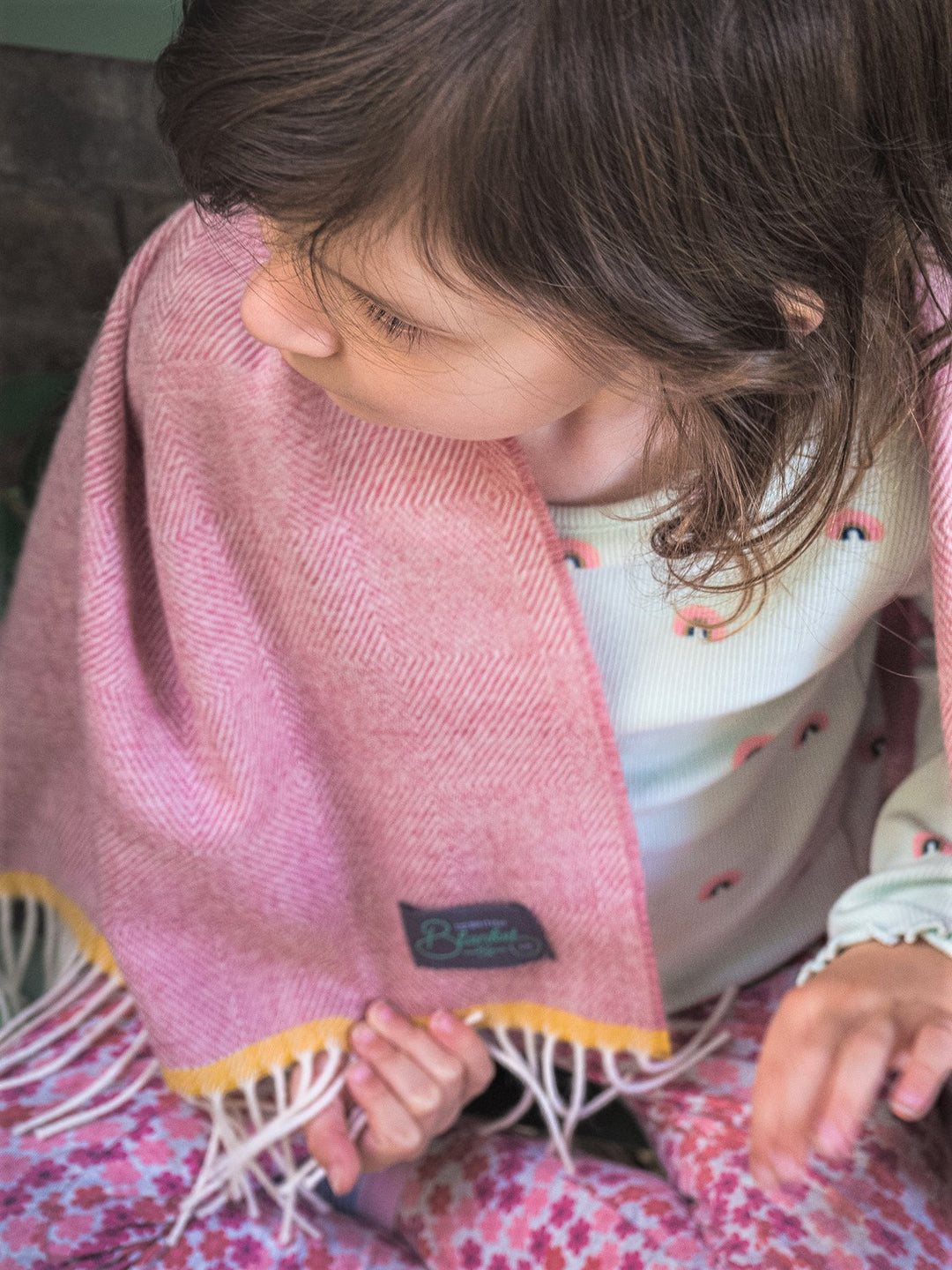 Pink merino lambswool baby blanket draped over a child's shoulder