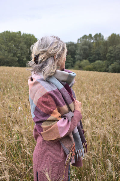A woman wrapped in an oversized purple and yellow wool scarf standing in a field. 
