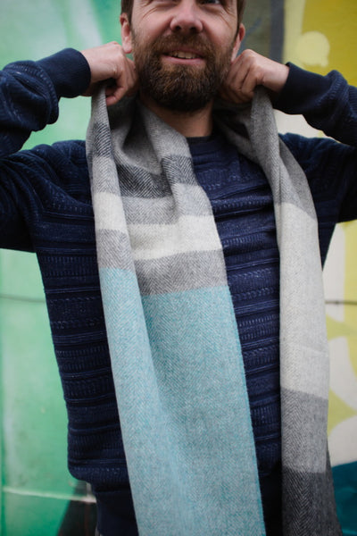 A man adjusting a grey and blue lambswool scarf hanging on his neck.