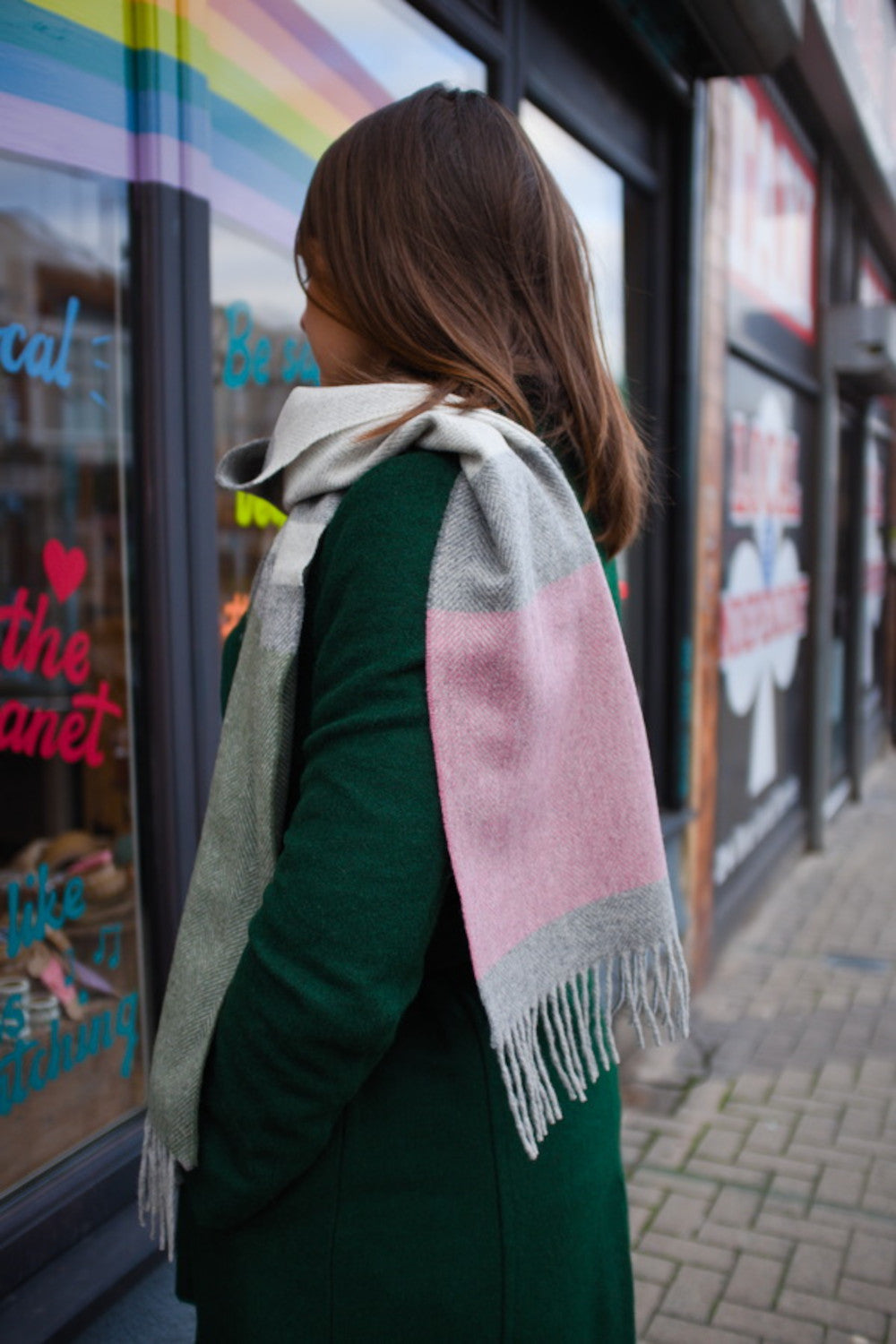 Side profile of a woman wearing a green, grey, and pink coloured lambswool scarf around her neck. 