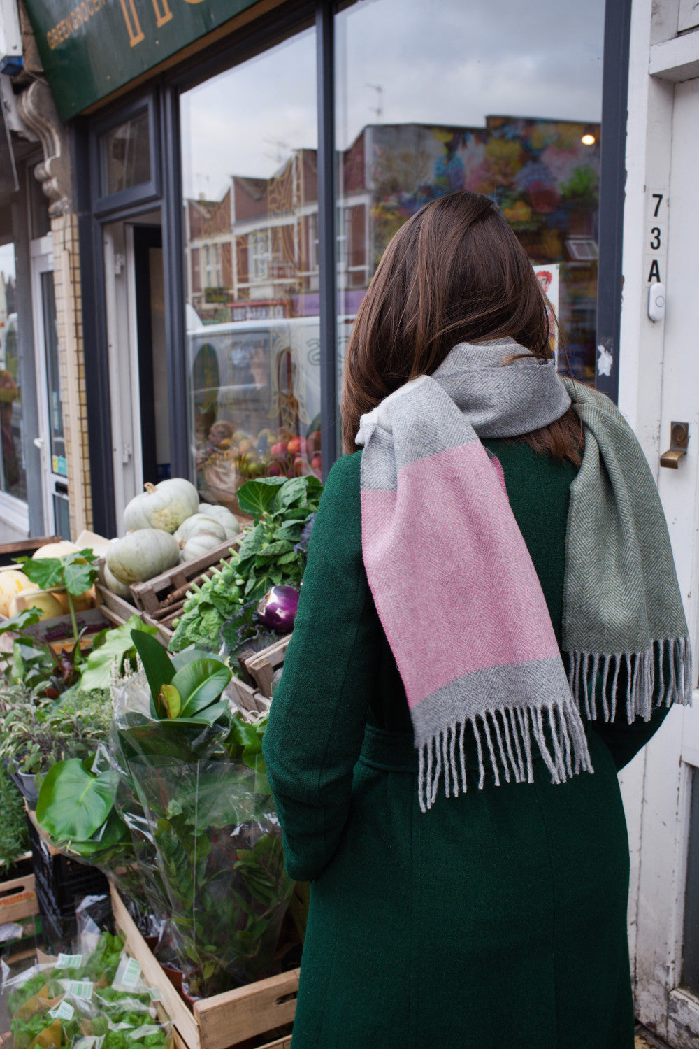 A woman wearing a green, grey, and pink coloured lambswool scarf around her neck with her back to the camera.