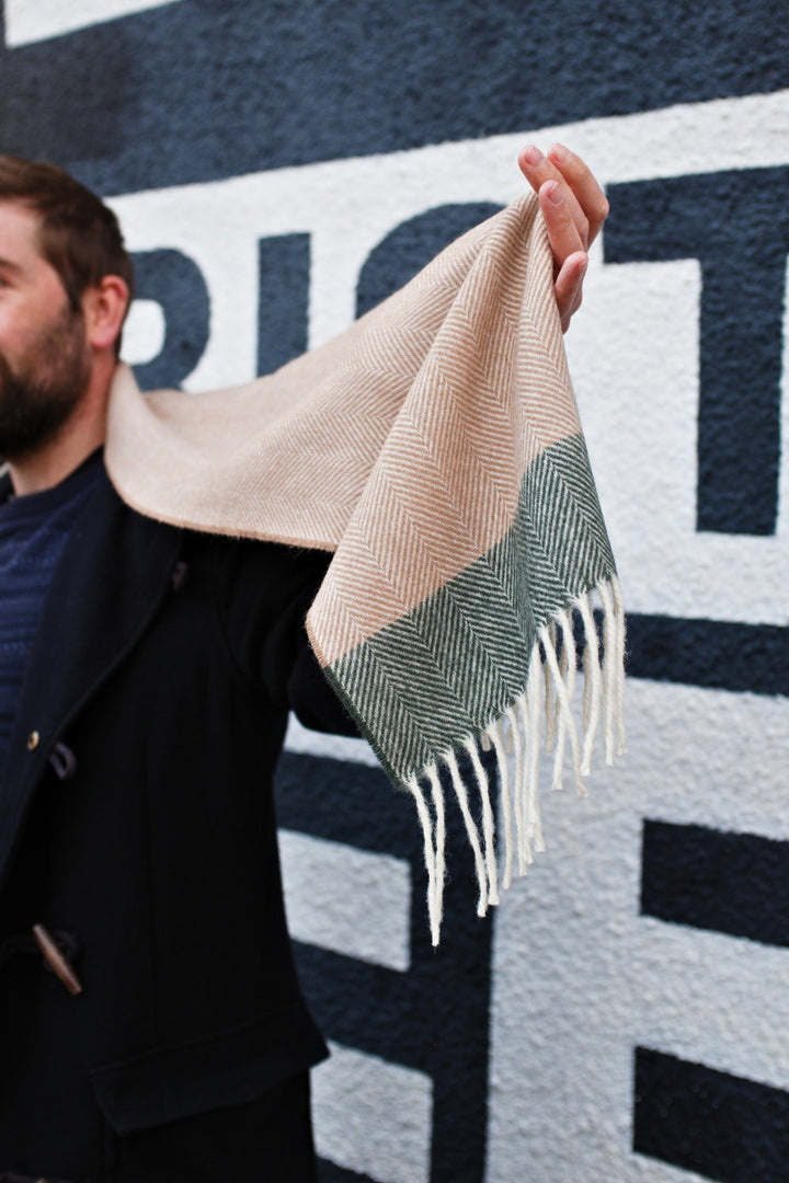 A man holding the edge of a beige and green lambswool scarf. 