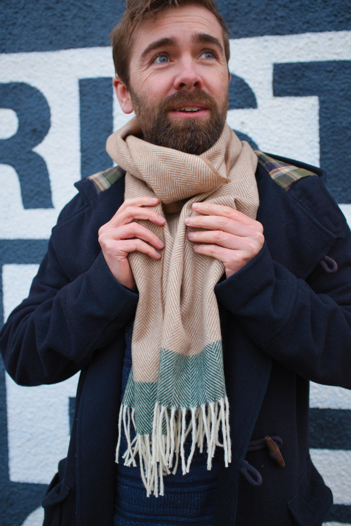 A man holding a beige and green lambswool scarf wrapped around his neck.