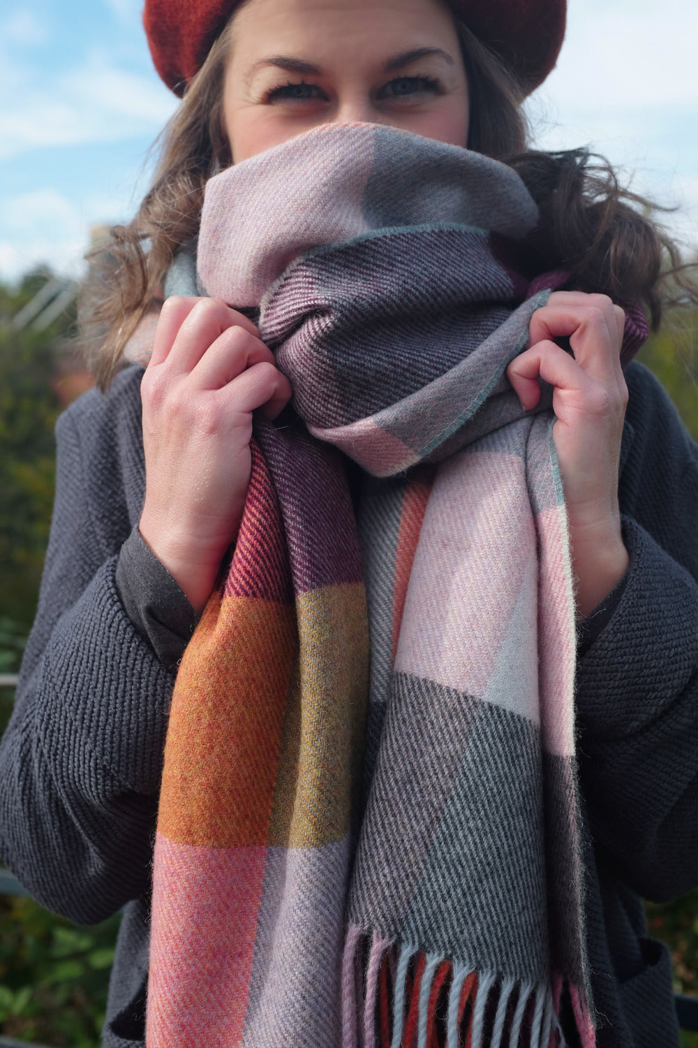 A woman wearing an oversized purple and yellow wool scarf. 