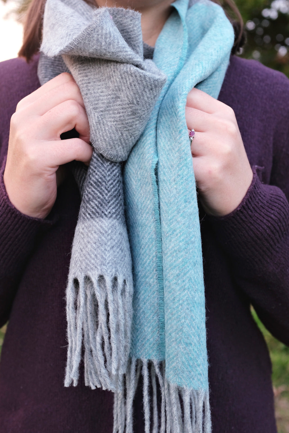 A woman holding a grey and blue lambswool scarf wrapped around her neck. 