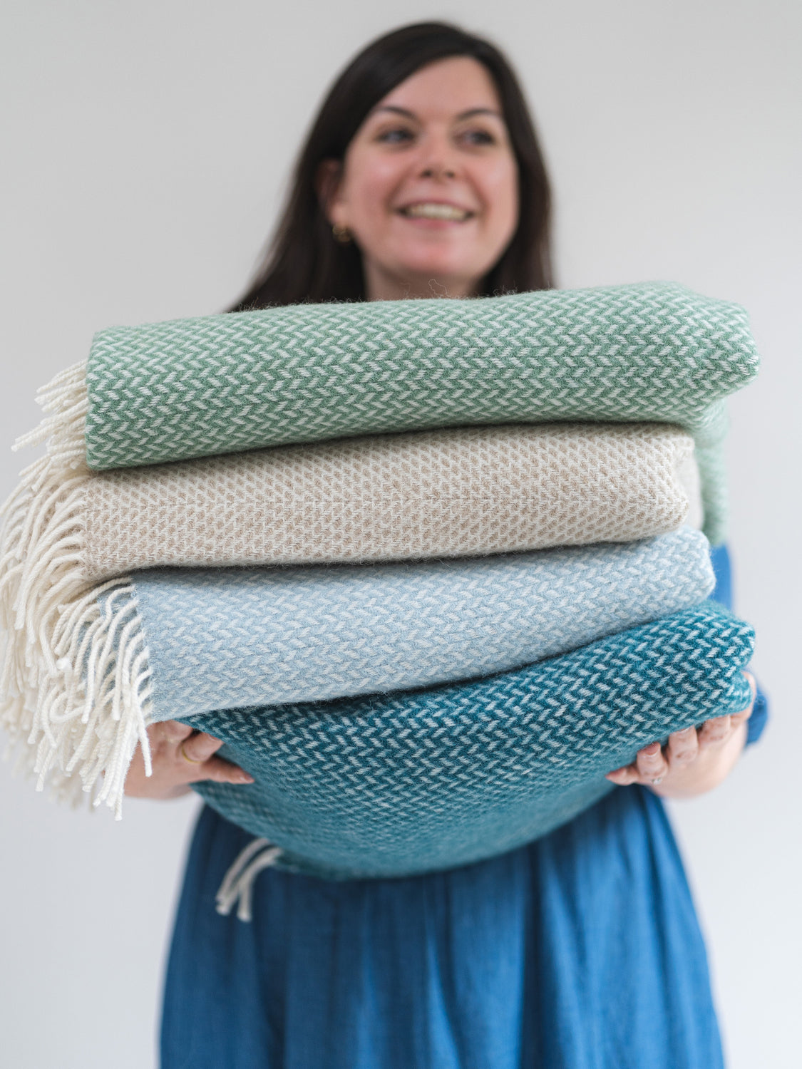 A woman holding out a stack of folded wool blankets in various colours