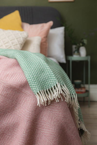 Green and pink wool throws hanging off the edge of a bed