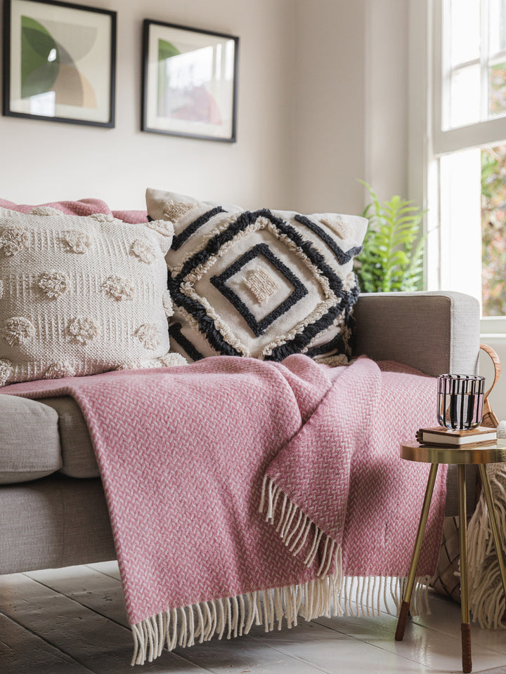 Large pink herringbone wool blanket on grey sofa underneath two cushions.