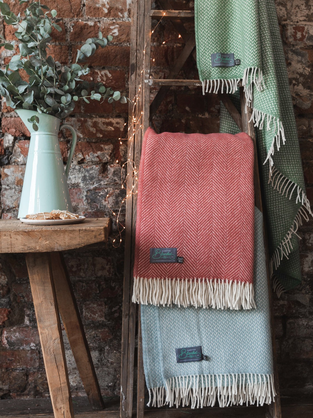 Three wool blankets in green, red, and blue hanging on a wooden ladder. 