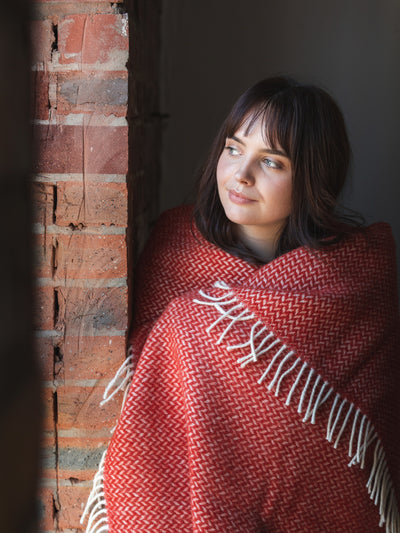 A woman looking to her right wrapped with an extra large red herringbone wool blanket