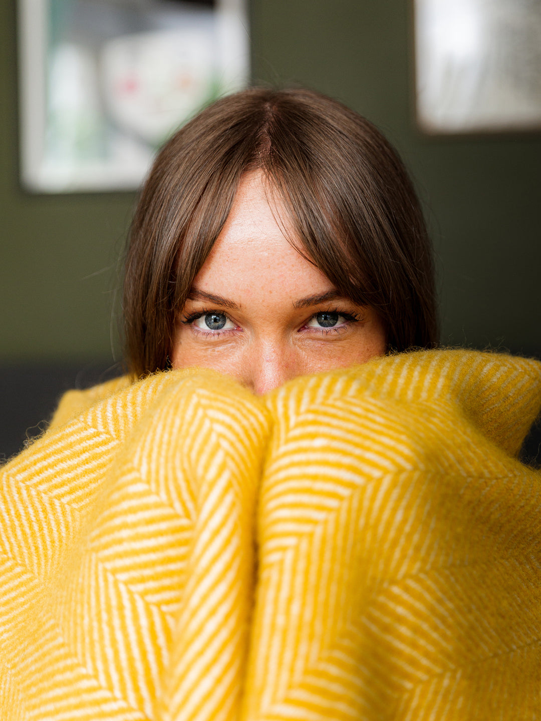 A woman covering her nose and mouth with a yellow herringbone wool blanket. 