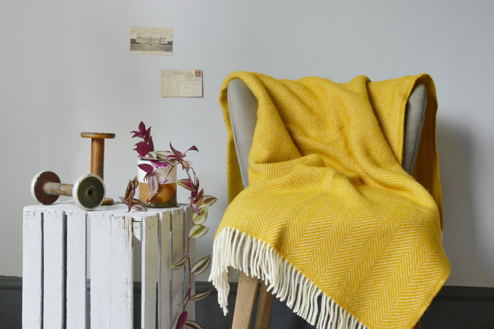 A yellow herringbone wool blanket draped over a lounge chair. 