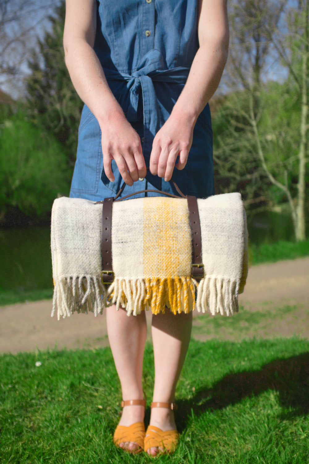 A woman holding the handle of leather straps carrying a yellow check wool picnic rug