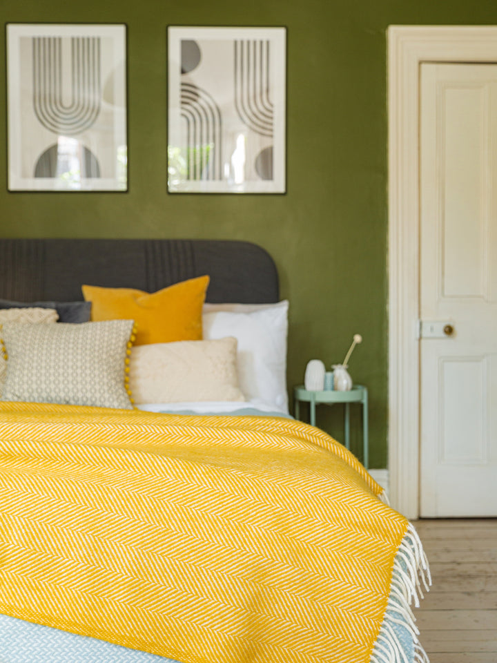 A large yellow herringbone wool throw on top of a bed. 