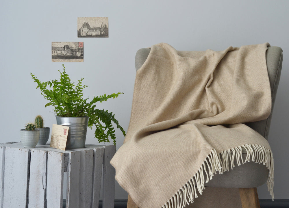 A beige herringbone throw draped over a lounge chair on the right with a wooden crate on its left. Various houseplants are on top of the wooden crate.