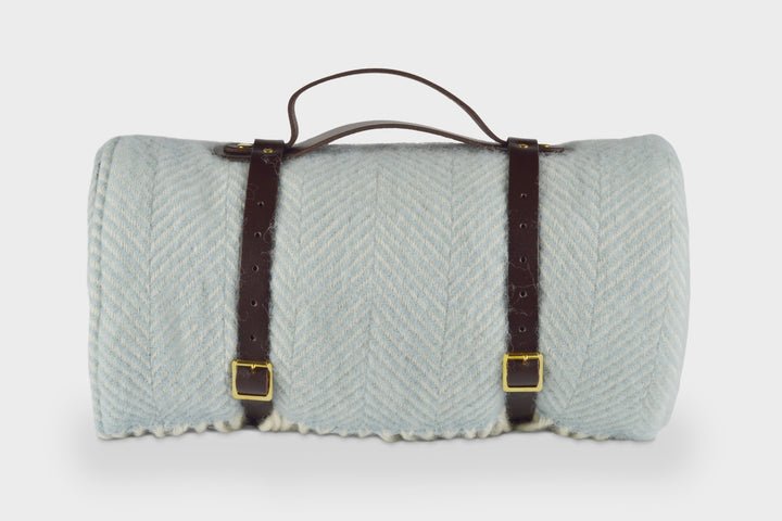 A blue picnic rug by The British Blanket Company rolled up with leather straps.
