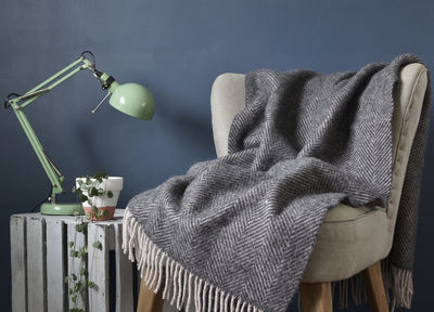 A grey herringbone wool blanket draped over a cream lounge chair. 