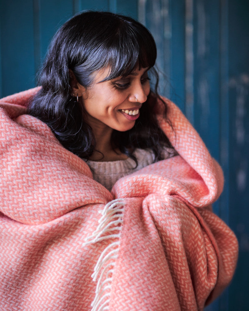 smiling woman wrapped in coral pink herringbone wool throw blanket by The British Blanket Company online shop