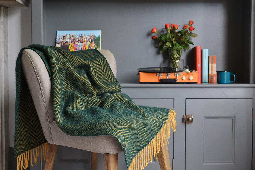 A green and yellow herringbone wool blanket draped over a grey lounge chair. 
