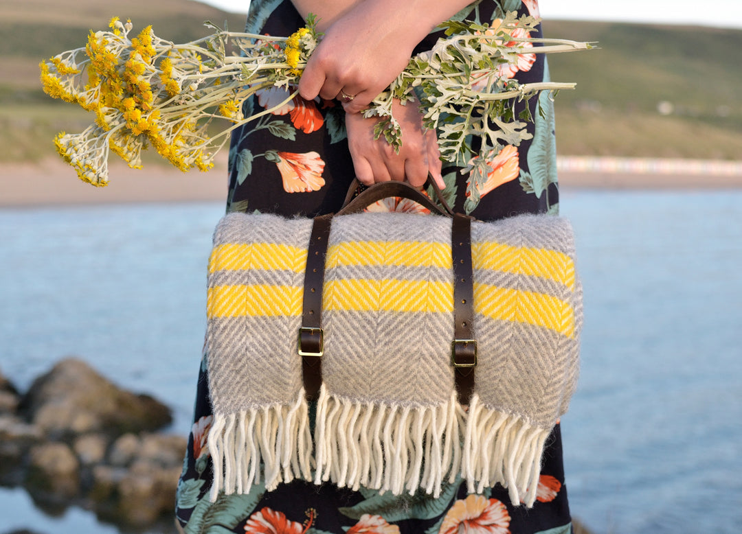 A woman holding a yellow and grey wool picnic rug rolled up with leather straps.