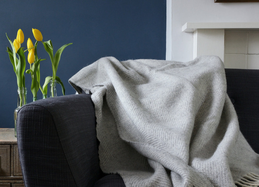 A large silver grey herringbone wool blanket draped over a sofa