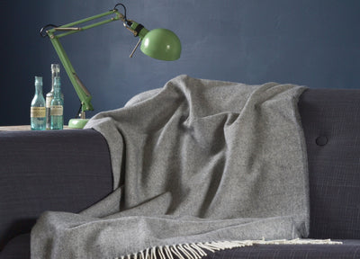 A large grey merino herringbone wool blanket is draped over a sofa