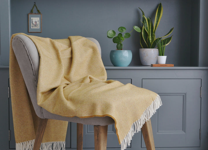Large yellow merino herringbone wool blanket draped over a lounge chair