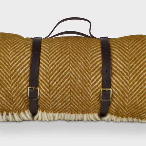 Yellow herringbone wool picnic rug by The British Blanket Company rolled up with leather straps