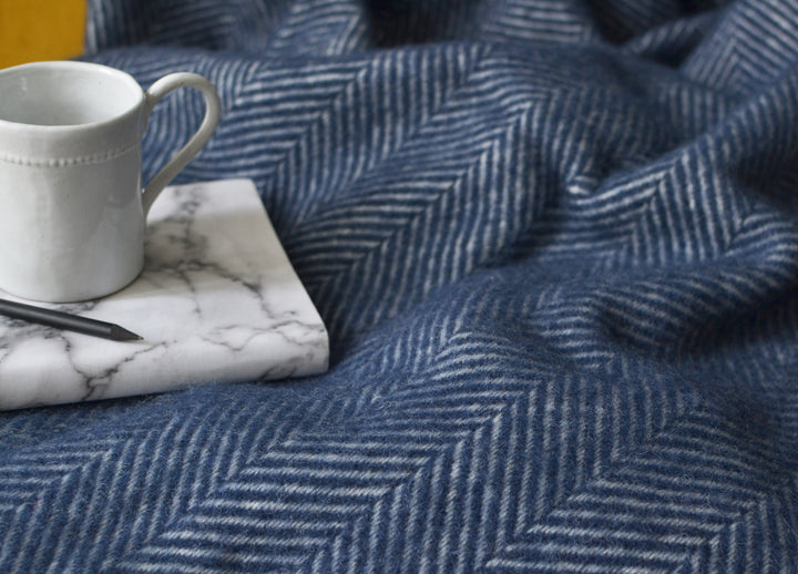 Closeup of a large navy blue herringbone wool throw with a mug and book on the left