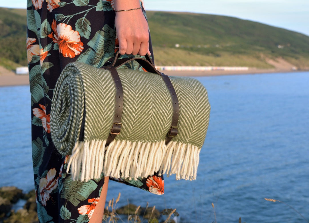 A person holding the handle for leather straps carrying a green wool picnic blanket