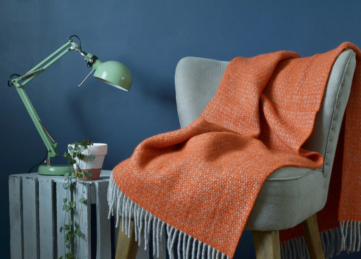 Orange and grey windmill wool blanket draped over a lounge chair on the right. A table lamp of ceramic pot are on a wooden crate on the left