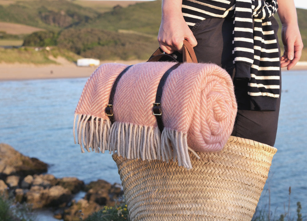 A person holding pink picnic blanket rolled up with leather straps. 