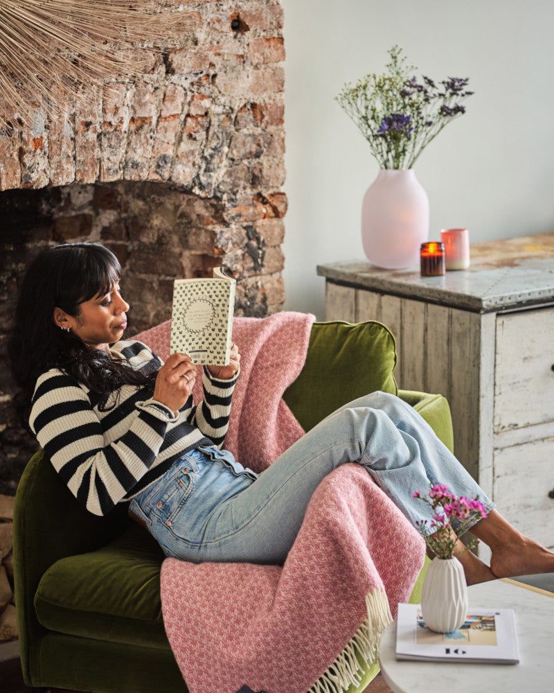 woman reading a book and sitting on a chair with a pink crescent pure wool throw blanket by The British Blanket Company online shop