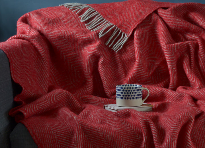 Large red and grey herringbone wool blanket draped over a sofa with a mug and book placed on top the blanket
