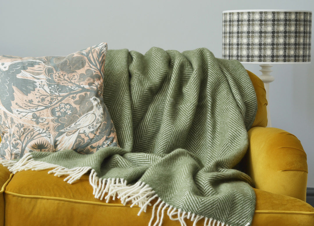 Large green herringbone wool blanket draped over a yellow sofa
