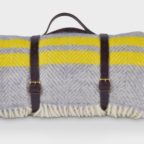 A yellow and grey wool picnic rug by The British Blanket Company rolled up with leather straps.
